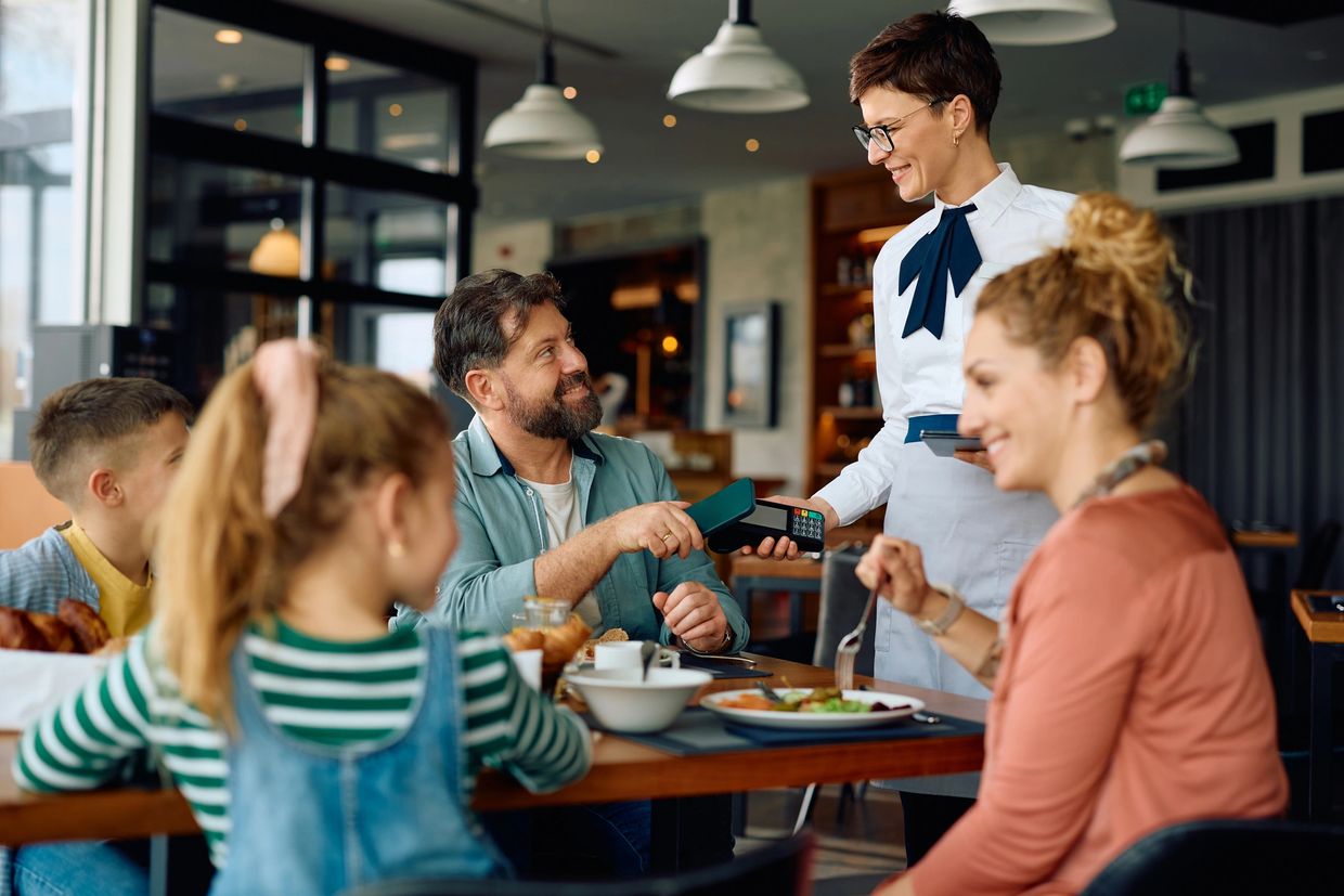 Family dining at a restaurant, man paying the bill with a card.