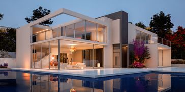 Modern two-story house with large glass windows and a pool.