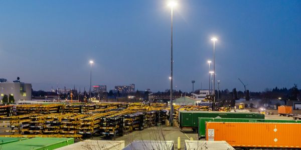 Industrial yard at dusk with stacked trailers and shipping containers under bright streetlights.