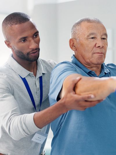 Physical therapist assists elderly man with arm exercises using dumbbells.