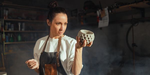 A woman inspects a textured ceramic pot in a workshop.