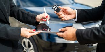 Person handing over car keys while another signs on a tablet.