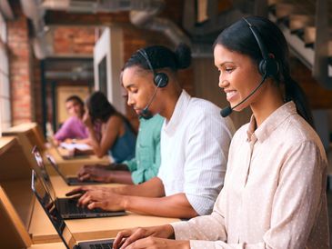 Call center workers wearing headsets and working on laptops in an office.