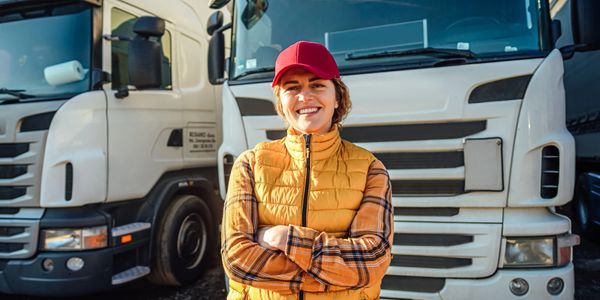 Smiling truck driver standing confidently in front of two trucks.