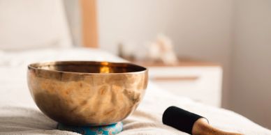A brass singing bowl on a soft surface with a wooden striker beside it.