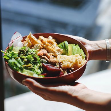 Hands holding a colorful, healthy salad bowl with greens, avocado, nuts, and chicken.