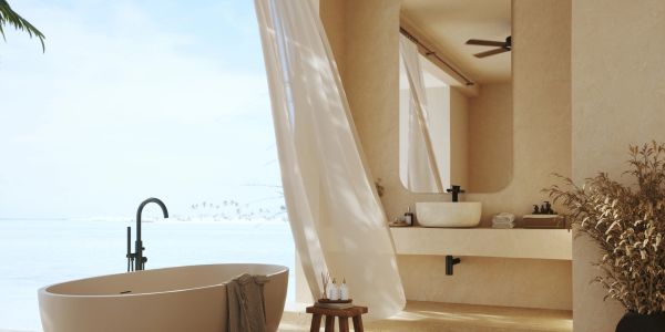 Elegant beige bathroom with a freestanding tub and flowing curtains overlooking the sea.