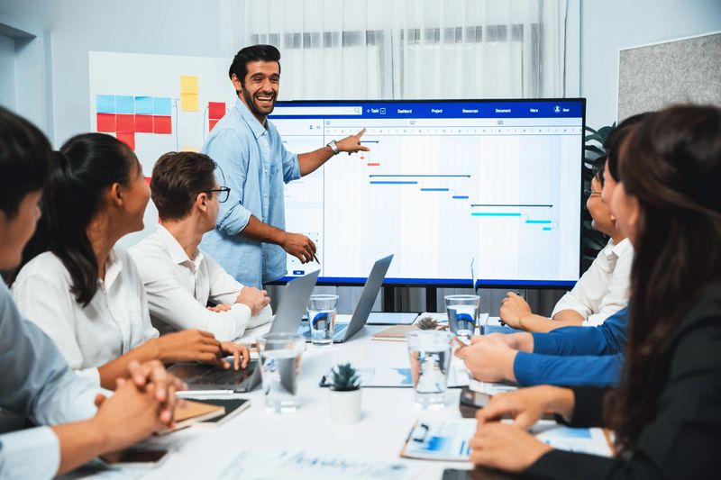 Project manager communicate and collaborate with team using project management software display on monitor, tracking progress of project task and making schedule plan at meeting table. Prudent