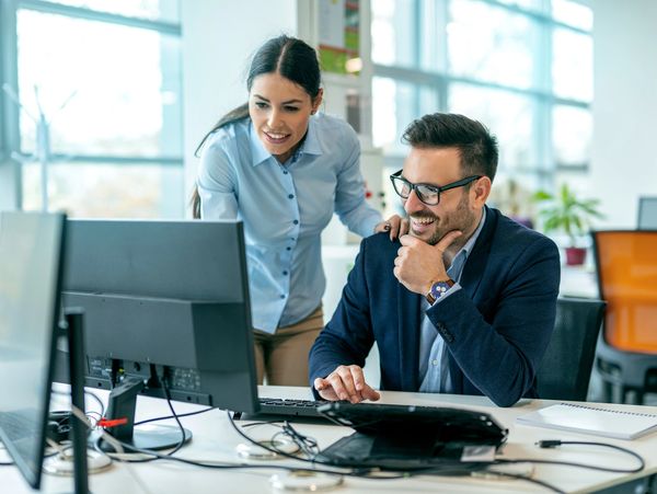 Two coworkers happily collaborating at a computer in a modern office.