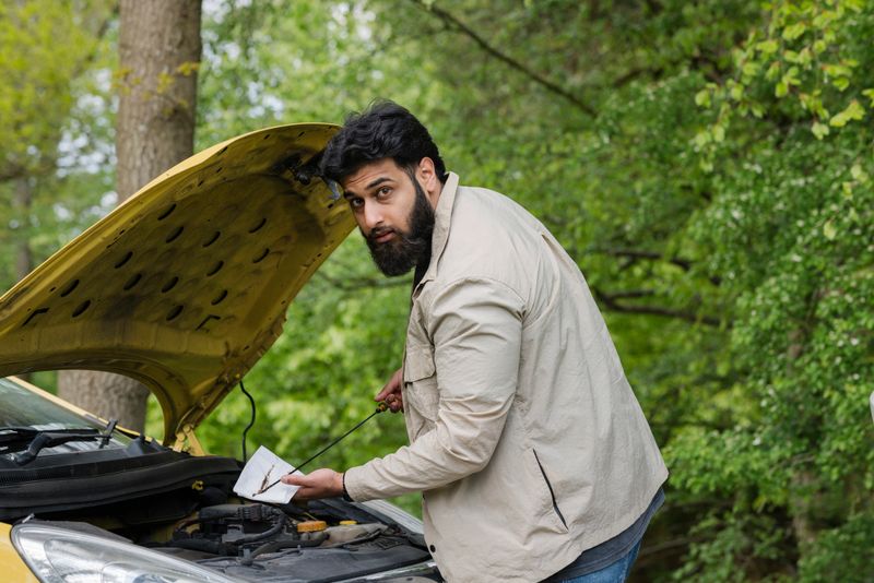 Man looking at the camera while checking the oil level in his car that has broken down. He is in Hexham, North East England.
