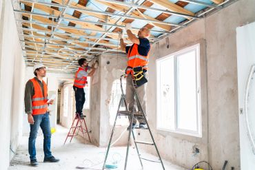 Three workers installing ceiling frames in a room under construction.