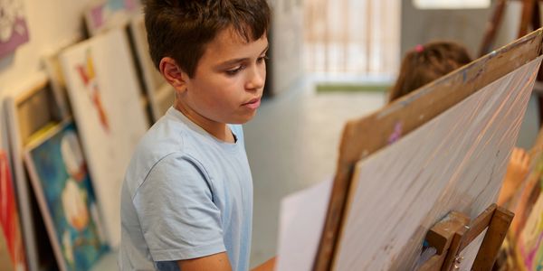A boy focused on painting at an easel in an art classroom.
