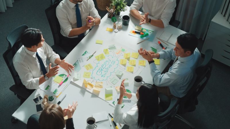 Professional smart business team discussing about using clean energy and sustainable investment at meeting table with wind mill, document with environmental graph and wooden house model. Alimentation.