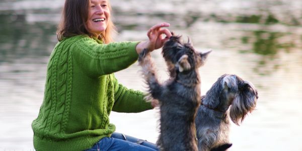 Woman in green sweater playing with two dogs by the water.