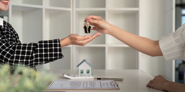 Person handing over house-shaped keychain with keys to another person.