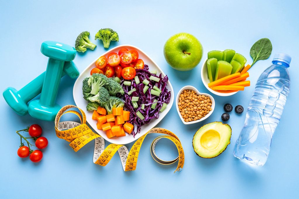 Healthy lifestyle essentials with fresh vegetables, fruits, water, dumbbells, and a measuring tape.