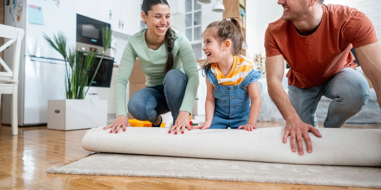 Family happily unrolling a rug together in their home.
