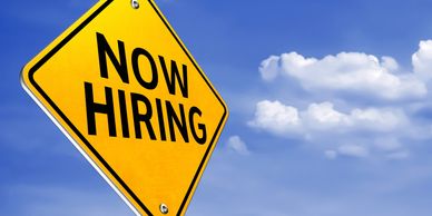 Yellow sign with 'NOW HIRING' against a blue sky.