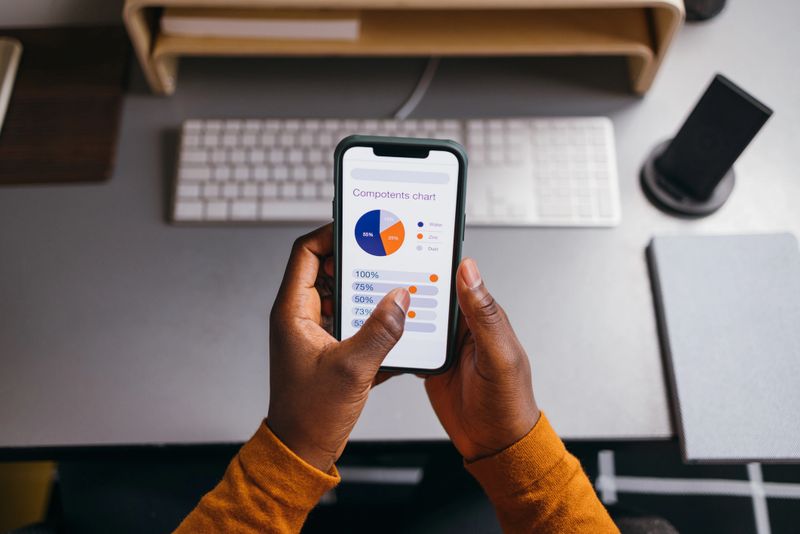 Hands holding phone displaying pie chart in office setting.
