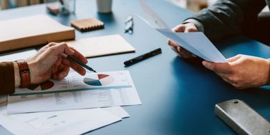 Two people discussing financial graphs and documents at a blue desk.
