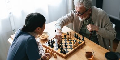 An elderly man and a woman enjoying a game of chess at a wooden table.