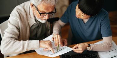 A caregiver assisting an elderly man with paperwork at a table.