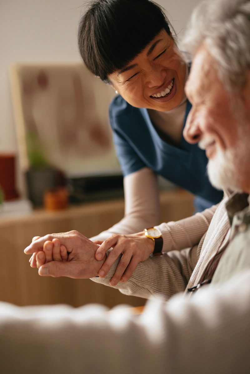 Cheerful smiling Japanese female caregiver talking and laughing with her unrecognizable elderly patient.