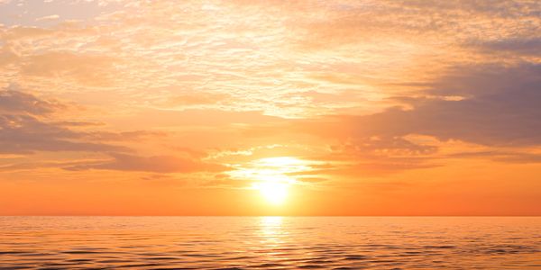 A serene sunset over calm ocean waters with a golden sky.