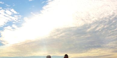 Two people sitting on chairs facing a bright sky and water.