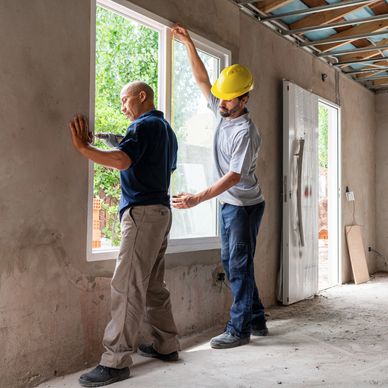 Two construction workers installing a window in a building under renovation.