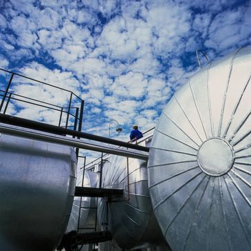 Industrial storage tanks under a cloudy blue sky with a worker on top.