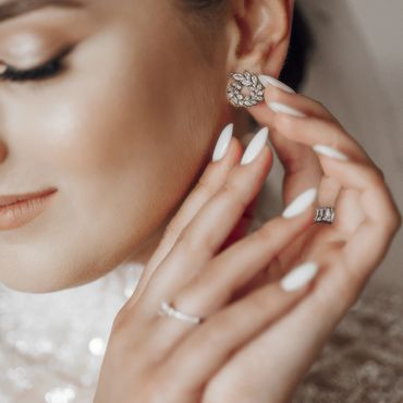 Close-up of a woman wearing elegant earrings and rings with manicured nails.
