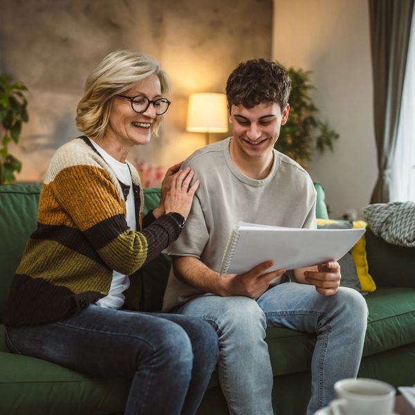 A woman and a young man happily review papers on a green couch.
