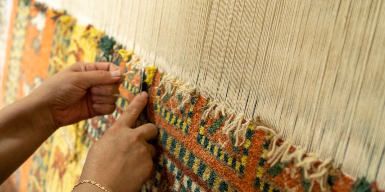Close-up of hands weaving a colorful carpet.