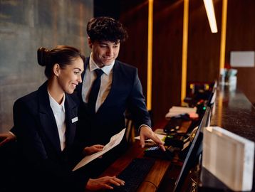Two hotel staff members working together at the front desk, reviewing documents.