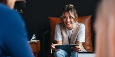 Smiling woman holding a tablet during a conversation in a cozy office setting.