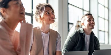 Three young professionals smiling and working on laptops in a bright office space.