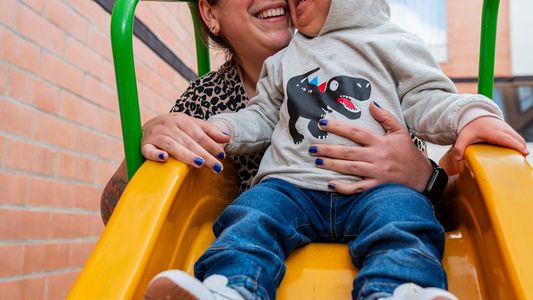 A joyful mother and child smiling together on a yellow slide outdoors.