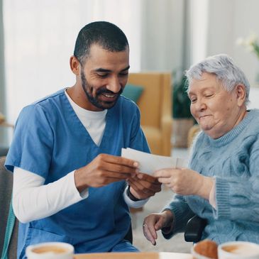 A caregiver and elderly woman looking at photos together in a cozy room.