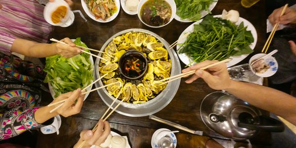 People enjoying a traditional hot pot meal with fresh vegetables and dipping sauces.