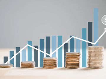 Stacks of coins with a rising financial graph and dollar symbol.