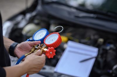 Person holding HVAC pressure gauges near a car engine.