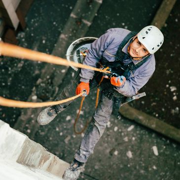 A worker rappelling down a building wearing safety gear and helmet.