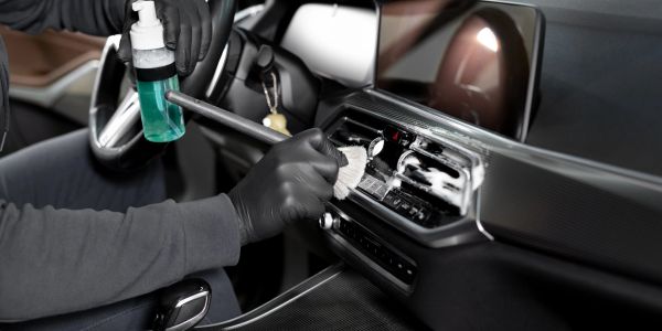 Person cleaning a car's dashboard with spray and cloth.