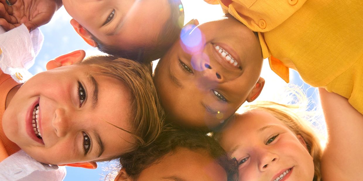 Group of happy children smiling together in a sunny outdoor setting.