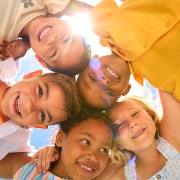 Group of happy children smiling in a circle under the sun.