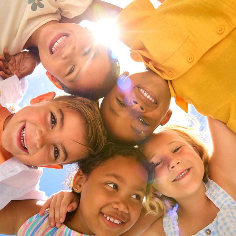 Group Of Multi-Cultural Children Friends Linking Arms Looking Down Into Camera