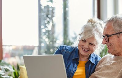 Elderly couple happily using a laptop together on a cozy couch.