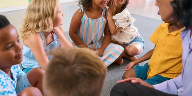 Children sitting in a circle, sharing secrets and smiling in a classroom.