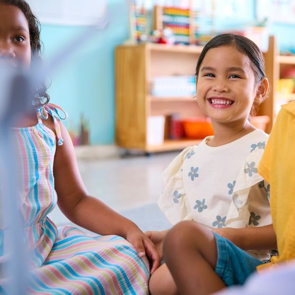 Children sitting together, one smiling brightly in a colorful classroom.